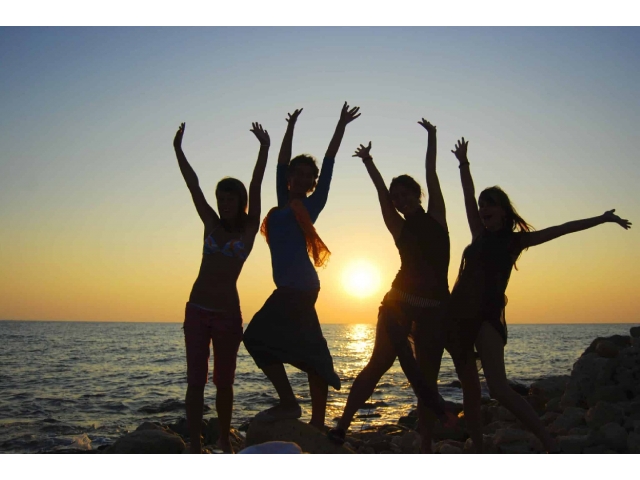the sillouette against the ocean and a setting sun of four women with their hands raised