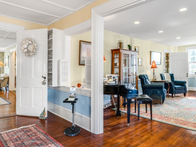 Elegant parlor and guest entrance with polished wood floors, vintage rugs, and a grand piano, offering a welcoming common area at the inn.