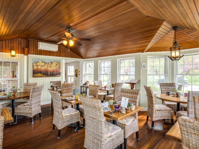 Bright and welcoming dining room with wicker chairs, wood floors, and a vaulted wood ceiling, filled with natural light from surrounding windows.