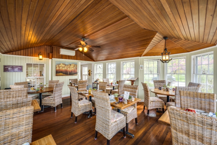 Bright and welcoming dining room with wicker chairs, wood floors, and a vaulted wood ceiling, filled with natural light from surrounding windows.