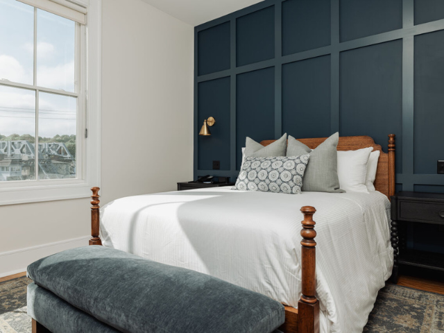 Elegant bedroom featuring a four-poster king bed, blue paneled accent wall, cozy seating, and ample natural light.