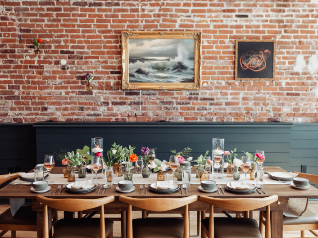 Decorated dining table with floral arrangements set against an exposed brick wall and maritime artwork.