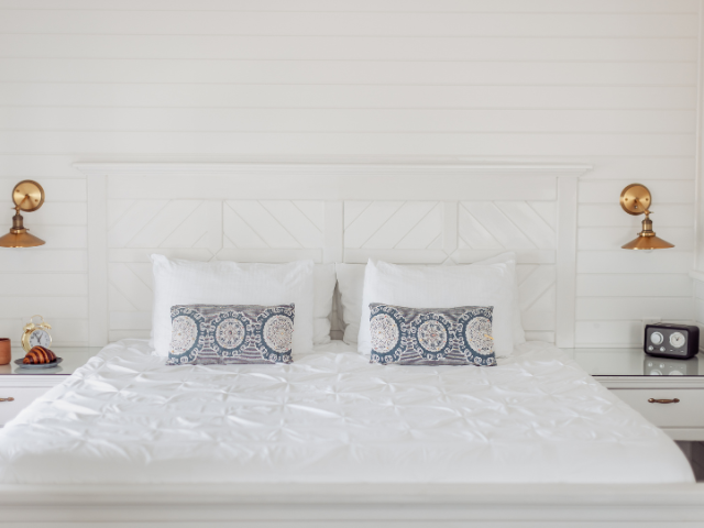 Bright and airy guest room with white linens, matching shiplap walls, brass sconces, and charming breakfast setup.
