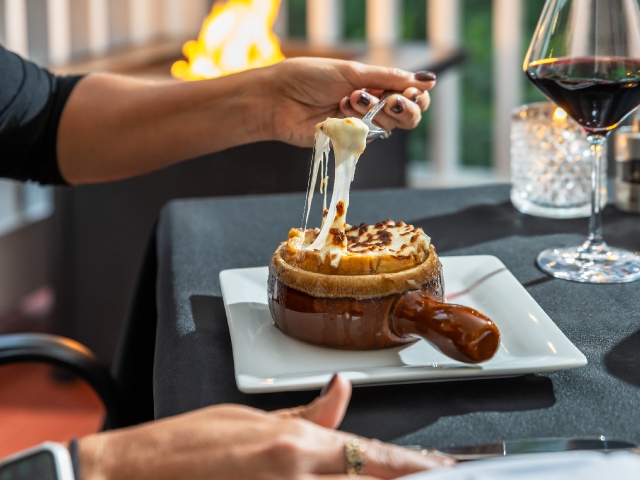 crock of soup with a person using the spoon with melted cheese
