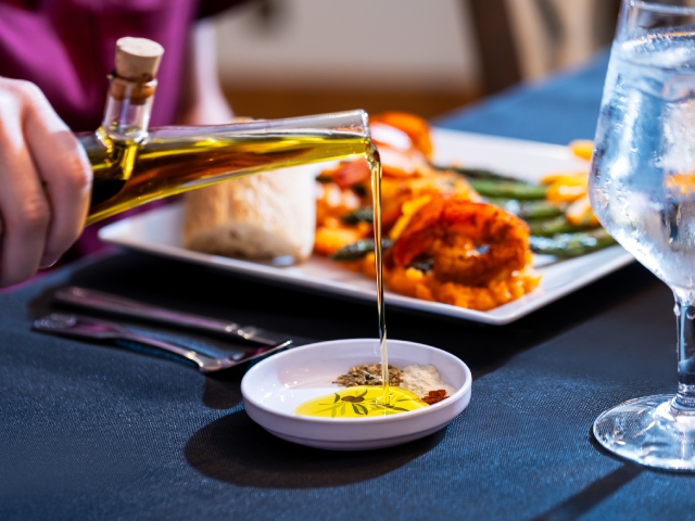 pouring olive oil from a dispenser into a cup with spices in front of a dinner