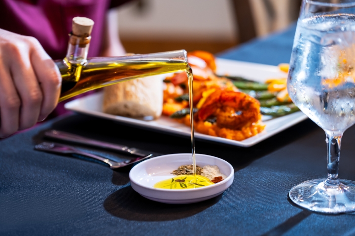 pouring olive oil from a dispenser into a cup with spices in front of a dinner