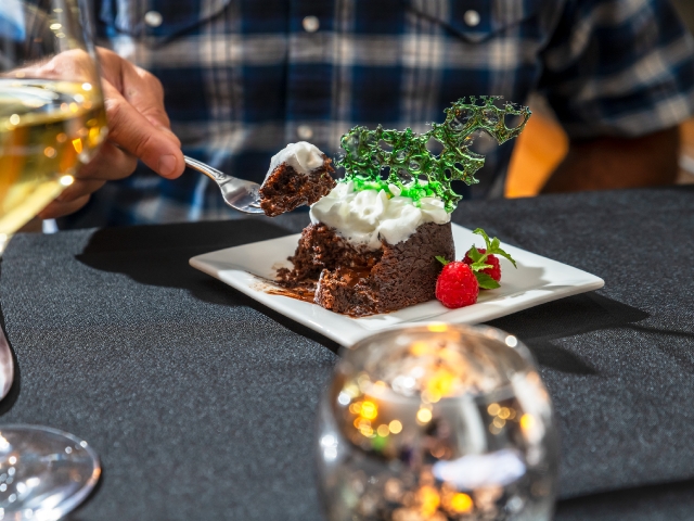 dinner table setting with someone taking a bite of a chocolate cake with whipped cream
