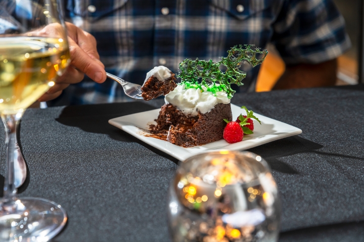 dinner table setting with someone taking a bite of a chocolate cake with whipped cream