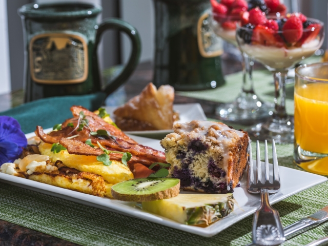 breakfast plate with omelet, bacon, blueberry cake and fresh fruit