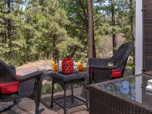 patio area in front of trees with rocking chairs and a table