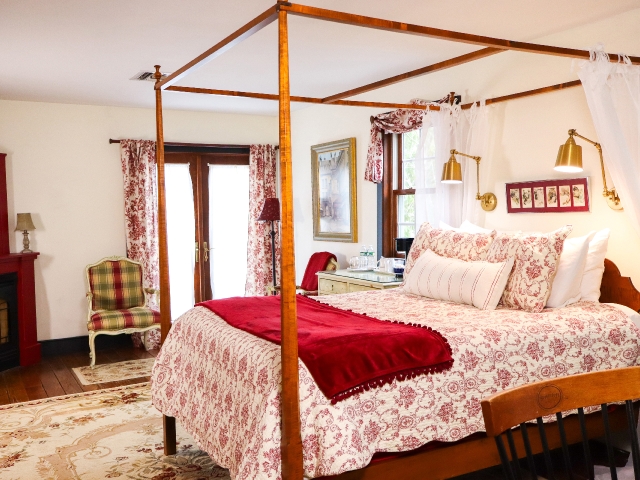 Four poster queen bed with red and white comforter and red blanket, and plaid chair