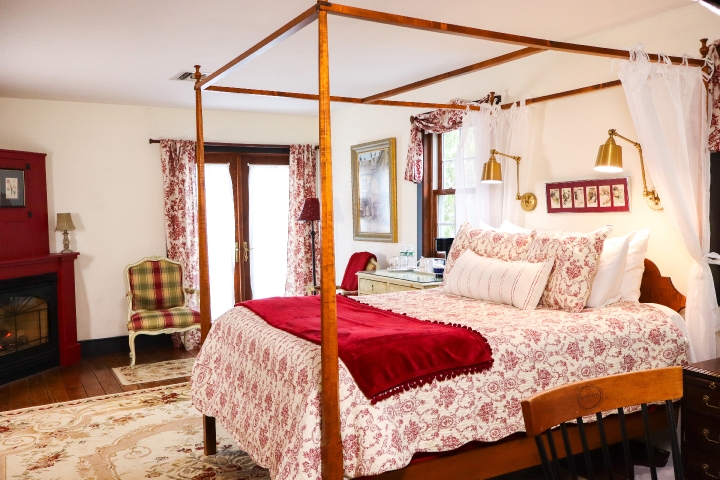 Four poster queen bed with red and white comforter and red blanket, and plaid chair