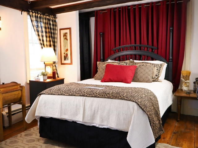 Queen nautical bed with white comforter, primitive blanket and red pillow with burgundy drapes