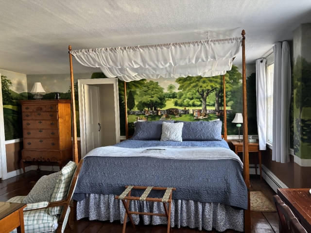King size four poster bed with canopy, blue bedspread and mural on the wall