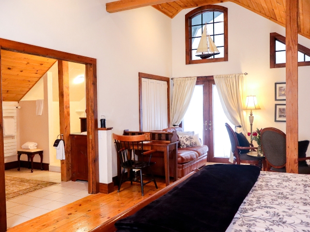 Cathedral ceiling room with part of a bed with desk, couch, chair and open door to a bathroom
