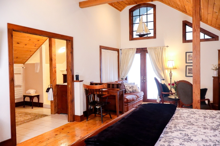 Cathedral ceiling room with part of a bed with desk, couch, chair and open door to a bathroom