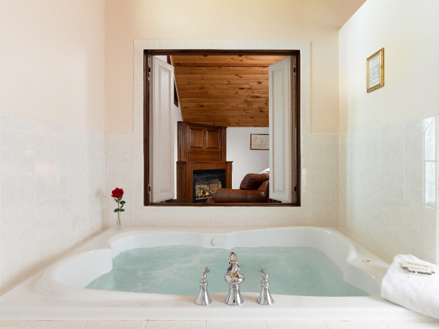 Jacuzzi tub with water and open shutters looking into a bedroom