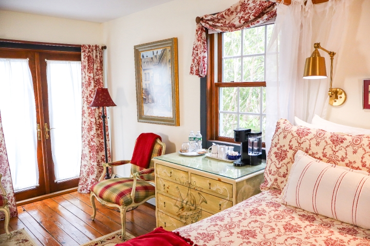 Red plaid chair with red blanket, dresser with a Keurig on top and part of a bed with a red and white pattern