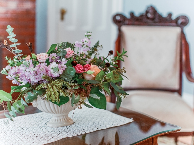 A vase of soft blooms resting on a lace‑draped table in the quiet parlor of Finger Lakes Bed and Breakfast at Hutton Farm.