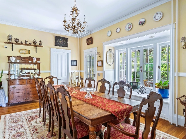 A historic dining room with a long wooden table, carved chairs, and soft daylight warming the timeless details.