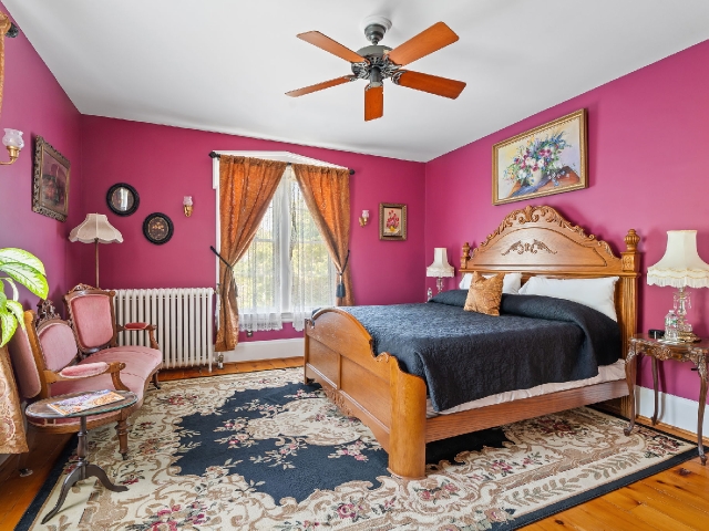 A richly colored historic guest room with an ornate wooden bed, vintage furnishings, and soft light warming the space.