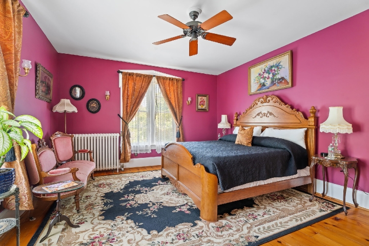 A richly colored historic guest room with an ornate wooden bed, vintage furnishings, and soft light warming the space.