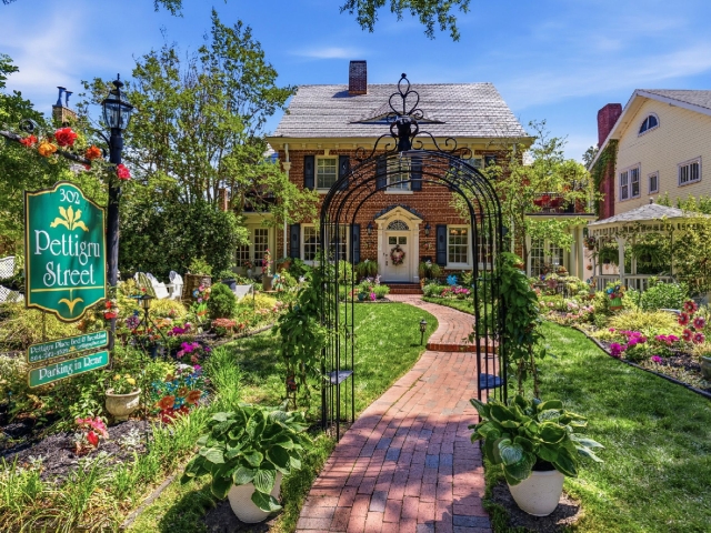 Red brick pathway through blooming garden to two story house.