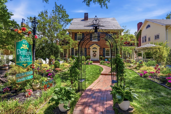 Red brick pathway through blooming garden to two story house.