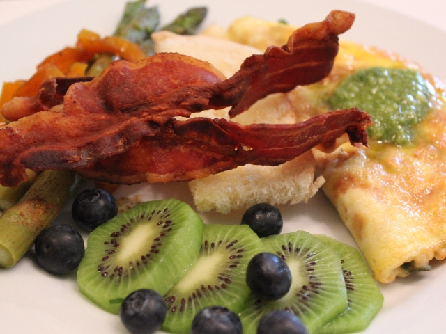 A fresh, home-cooked breakfast at Prairie Guest House featuring a garden omelet topped with pesto, served with kiwi, blueberries, fresh vegetables, and crisp bacon.