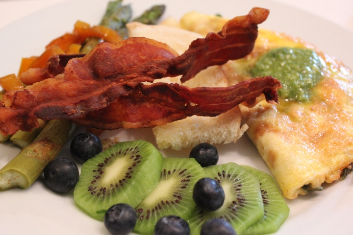 A fresh, home-cooked breakfast at Prairie Guest House featuring a garden omelet topped with pesto, served with kiwi, blueberries, fresh vegetables, and crisp bacon.