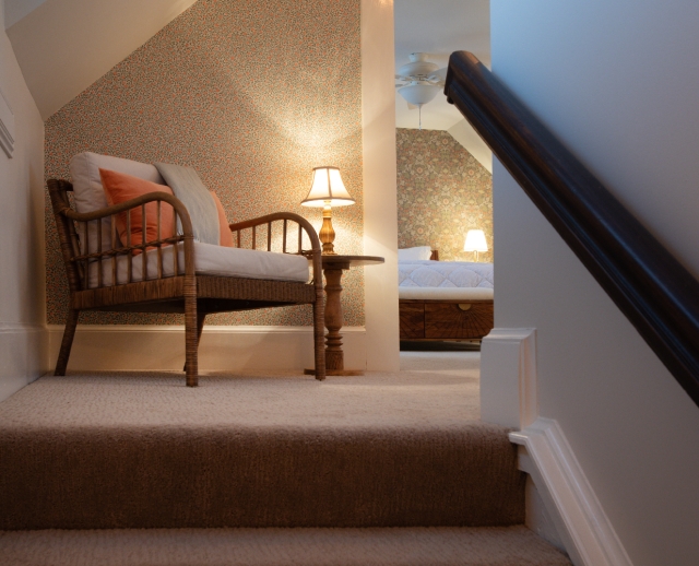 Cozy sitting area in the Honeymoon Suite, warmly illuminated by a lamp, with a glimpse of the bedroom and king-size bed beyond.