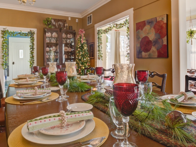 Festively decorated dining room at Prairie Guest House, featuring the historic mahogany L. S. Ayres dining table set with glowing candles, evergreen accents, and red goblets, with a Christmas tree twinkling in the background.