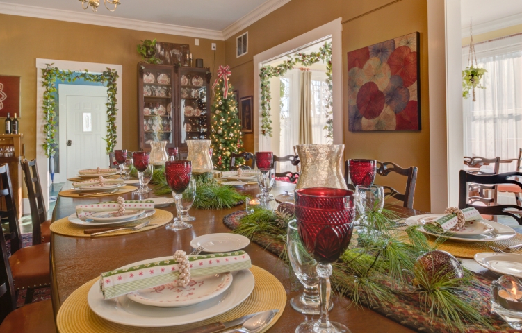 Festively decorated dining room at Prairie Guest House, featuring the historic mahogany L. S. Ayres dining table set with glowing candles, evergreen accents, and red goblets, with a Christmas tree twinkling in the background.