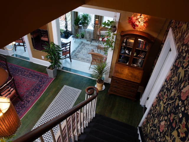 A graceful staircase leads down from the Honeymoon Suite, offering a glimpse of the welcoming dining room and sunlit sunroom below.