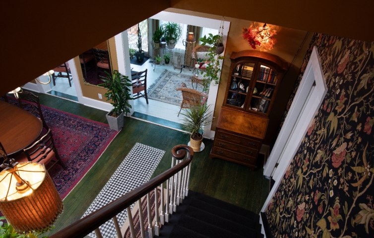 A graceful staircase leads down from the Honeymoon Suite, offering a glimpse of the welcoming dining room and sunlit sunroom below.