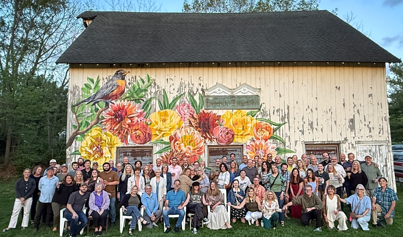 Guests gather for a special birthday celebration and pose for a photo in front of the hand-painted barn mural, surrounded by native trees in our lush green meadow.