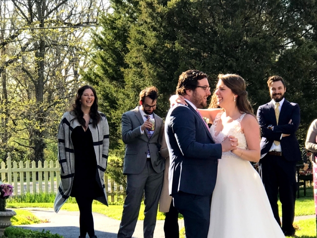 A radiant bride and groom share a joyful laugh in the beautiful courtyard gardens, surrounded by family and friends on their wedding day.